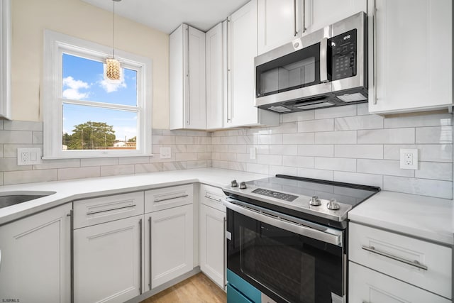 kitchen featuring decorative backsplash, decorative light fixtures, light countertops, stainless steel appliances, and white cabinetry