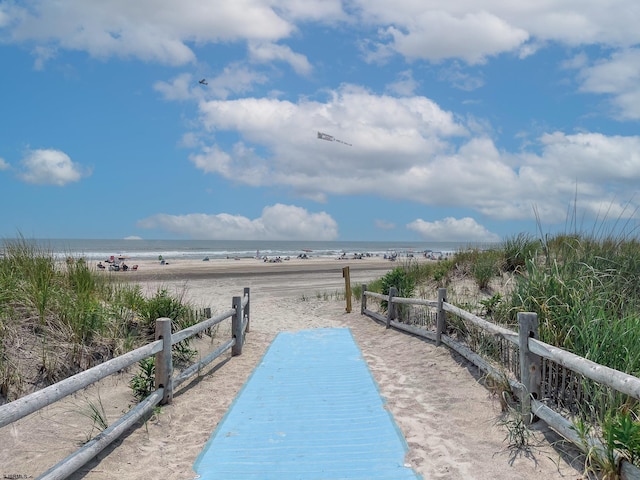 view of property's community featuring a view of the beach, a water view, and fence