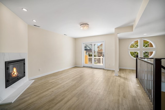 unfurnished living room featuring light wood-style flooring, visible vents, baseboards, and a high end fireplace