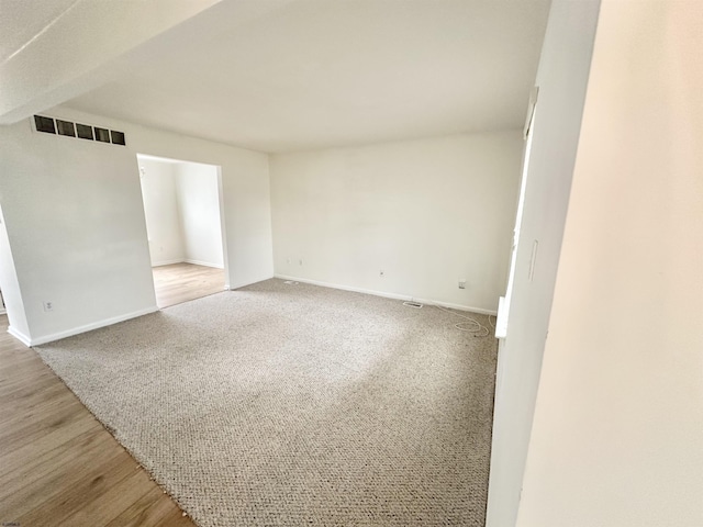 empty room featuring light wood finished floors, baseboards, visible vents, and light colored carpet