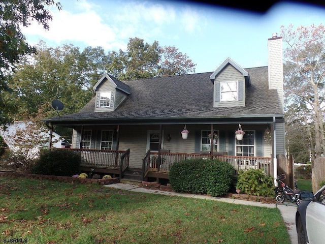 view of front of property featuring covered porch, roof with shingles, a chimney, and a front yard