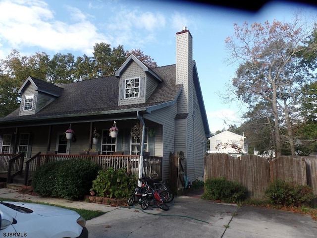 view of front of house with a shingled roof, a chimney, fence, and a porch