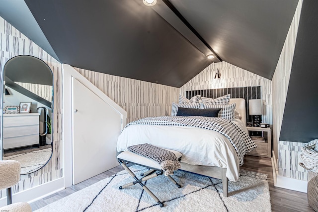 bedroom featuring lofted ceiling, wood finished floors, and wallpapered walls