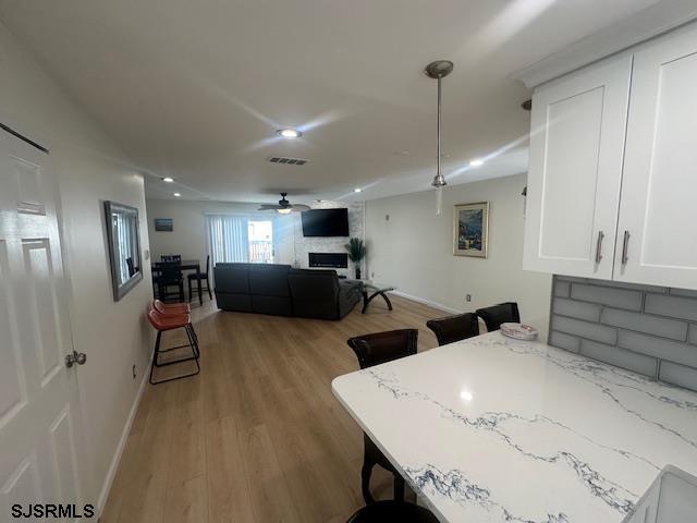 kitchen featuring a fireplace, visible vents, light wood-style flooring, white cabinets, and light stone countertops