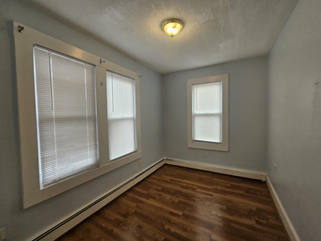 spare room featuring a baseboard heating unit, a wealth of natural light, dark wood finished floors, and baseboards