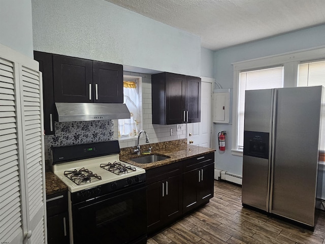 kitchen featuring stainless steel fridge, gas range, a baseboard radiator, under cabinet range hood, and a sink