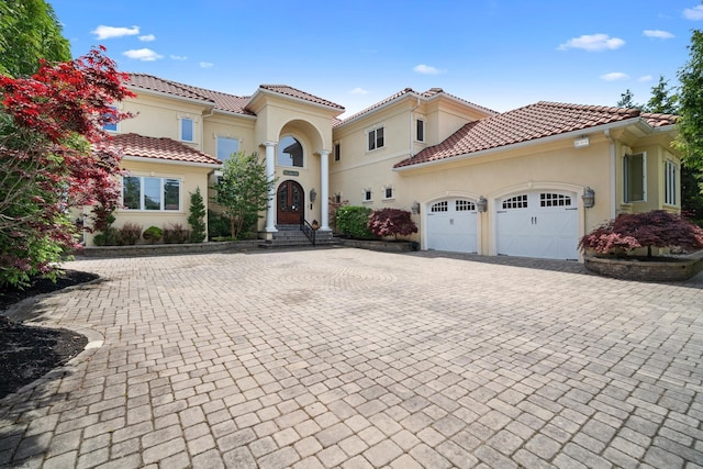 mediterranean / spanish home with an attached garage, a tiled roof, decorative driveway, and stucco siding