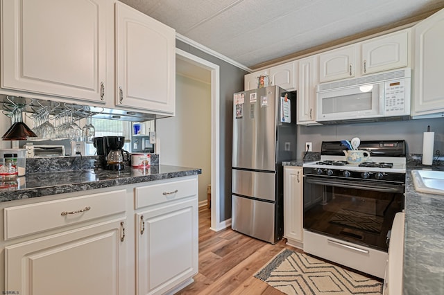 kitchen featuring white microwave, light wood-style floors, white cabinets, freestanding refrigerator, and gas range oven