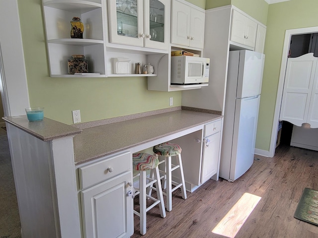 kitchen featuring built in desk, light wood finished floors, open shelves, white cabinets, and white appliances