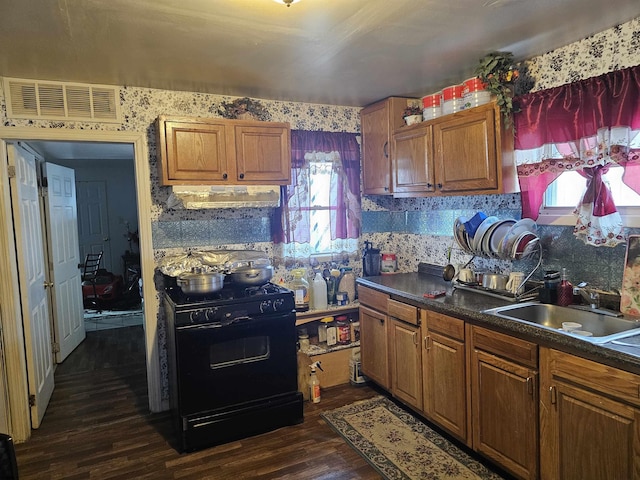 kitchen with visible vents, dark wood-type flooring, range hood, black range with gas stovetop, and a sink