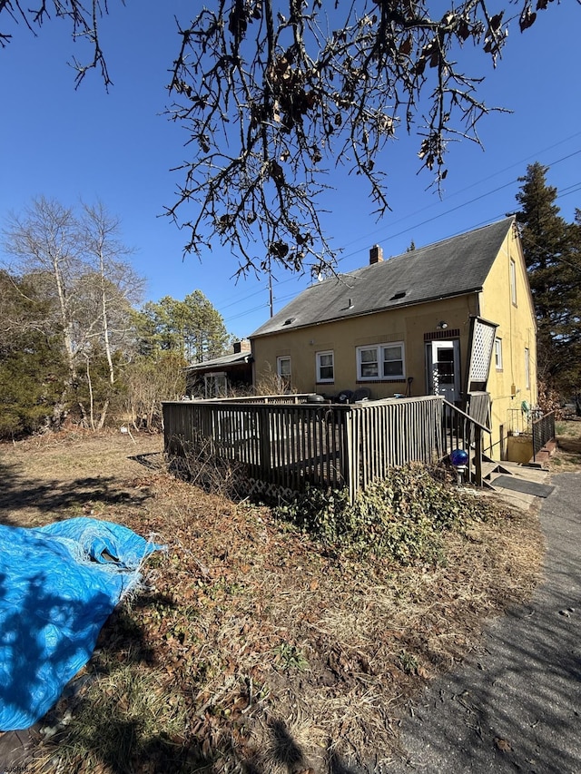 rear view of property featuring a chimney, a wooden deck, and stucco siding