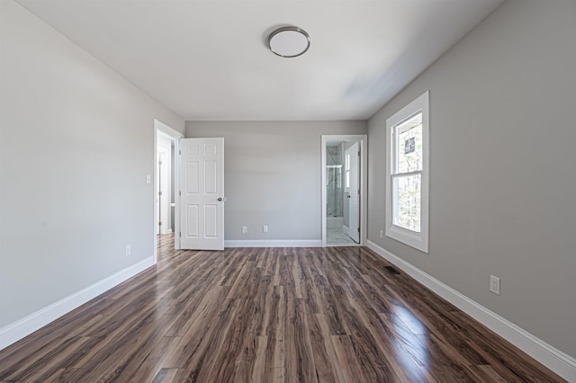 unfurnished bedroom featuring dark wood-type flooring, visible vents, connected bathroom, and baseboards