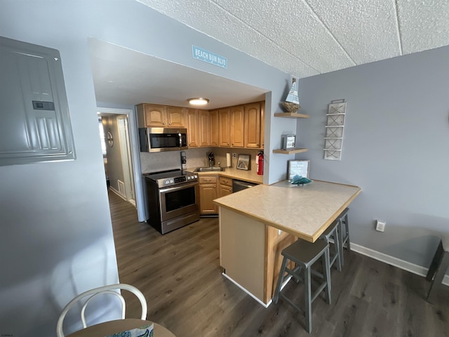 kitchen with a breakfast bar area, a peninsula, dark wood-type flooring, light countertops, and appliances with stainless steel finishes