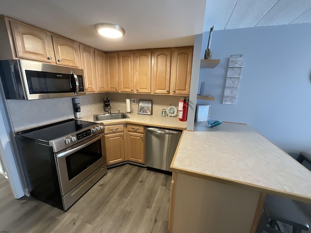 kitchen featuring light wood finished floors, appliances with stainless steel finishes, light brown cabinets, a sink, and a peninsula