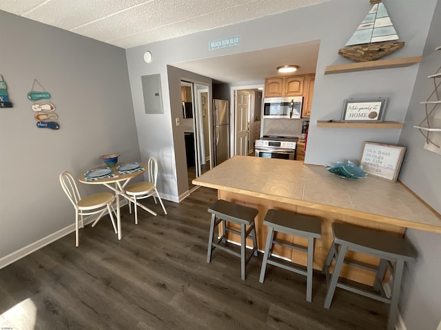 kitchen featuring dark wood-style flooring, stainless steel appliances, electric panel, a peninsula, and a kitchen bar