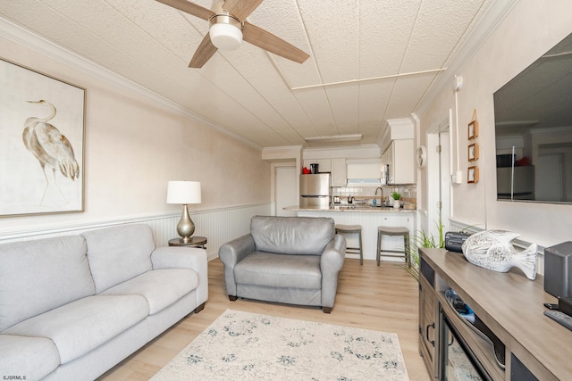 living room featuring ornamental molding, wainscoting, ceiling fan, and light wood finished floors