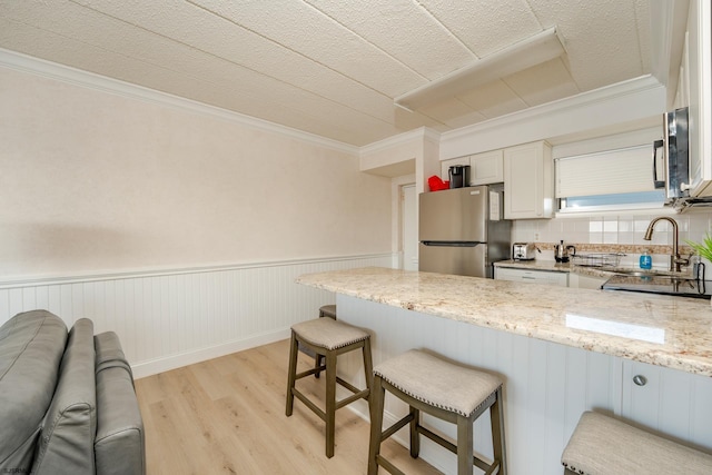 kitchen with a wainscoted wall, light wood-style flooring, freestanding refrigerator, a peninsula, and light stone countertops