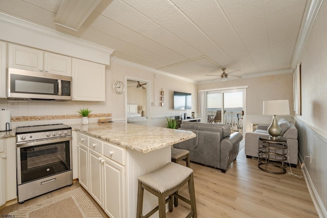 kitchen featuring a wainscoted wall, a peninsula, open floor plan, appliances with stainless steel finishes, and light wood finished floors