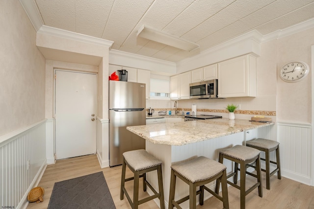 kitchen with a peninsula, white cabinetry, appliances with stainless steel finishes, and wainscoting