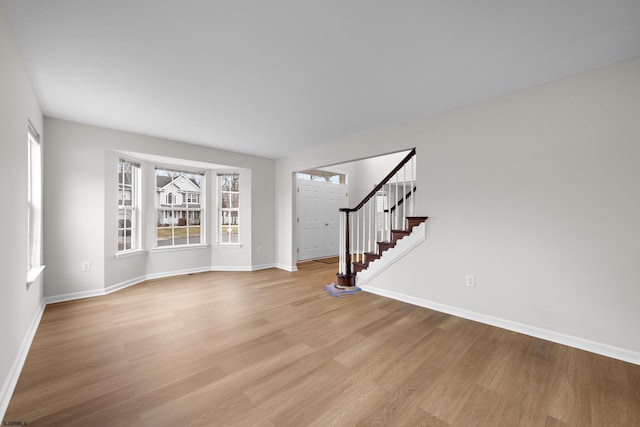 unfurnished room with light wood finished floors, baseboards, and stairway