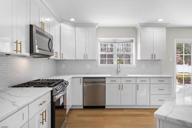 kitchen featuring light stone counters, light wood finished floors, stainless steel appliances, white cabinetry, and a sink