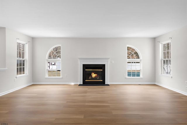 unfurnished living room featuring a fireplace with flush hearth, wood finished floors, a wealth of natural light, and baseboards