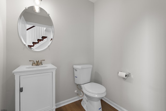 half bath with wood finished floors, vanity, toilet, and baseboards