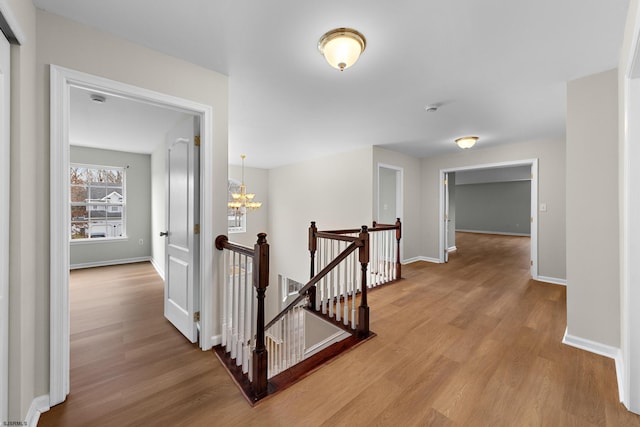 corridor featuring a notable chandelier, wood finished floors, visible vents, an upstairs landing, and baseboards