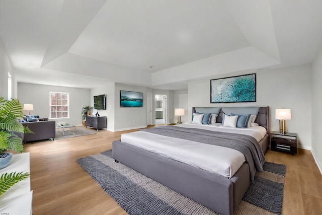 bedroom with light wood-style floors, a raised ceiling, and baseboards