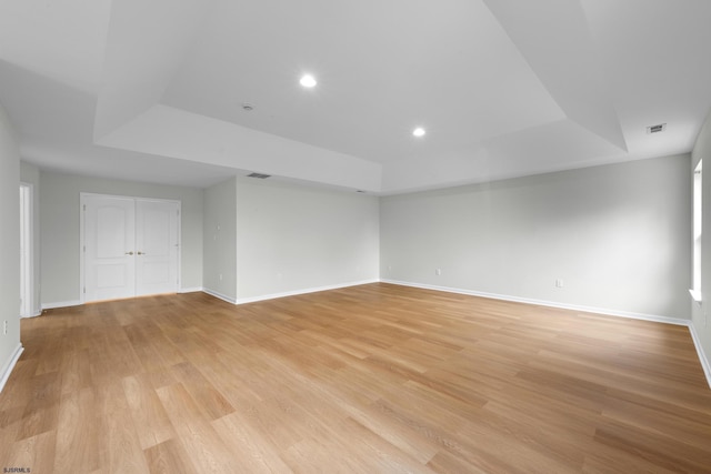empty room with a tray ceiling, visible vents, light wood-style flooring, and baseboards