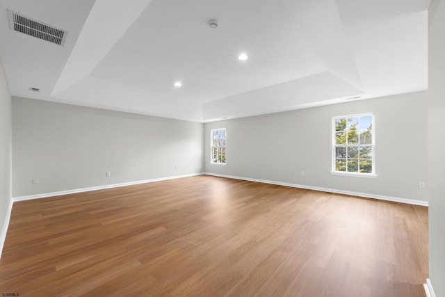empty room with light wood finished floors, a raised ceiling, and visible vents