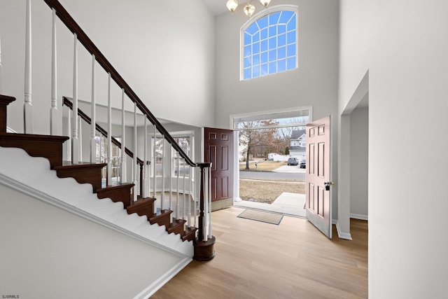 entrance foyer featuring a high ceiling, an inviting chandelier, wood finished floors, baseboards, and stairs