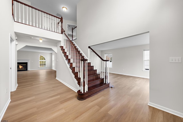 stairway featuring a warm lit fireplace, a high ceiling, baseboards, and wood finished floors