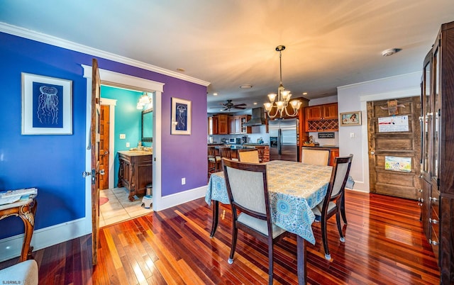 dining area with dark wood-style floors, crown molding, baseboards, and ceiling fan with notable chandelier