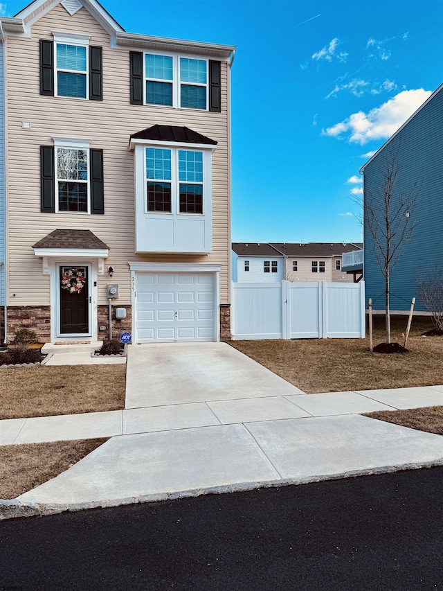 view of front of home featuring a garage, fence, driveway, stone siding, and a gate