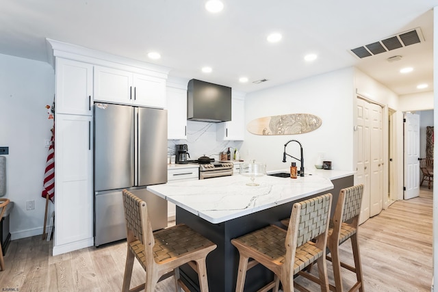 kitchen featuring a kitchen bar, visible vents, appliances with stainless steel finishes, a sink, and wall chimney exhaust hood