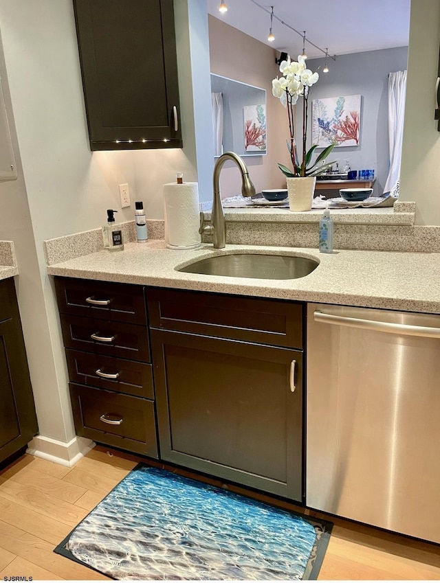 kitchen with light wood finished floors, dark brown cabinetry, light stone countertops, stainless steel dishwasher, and a sink