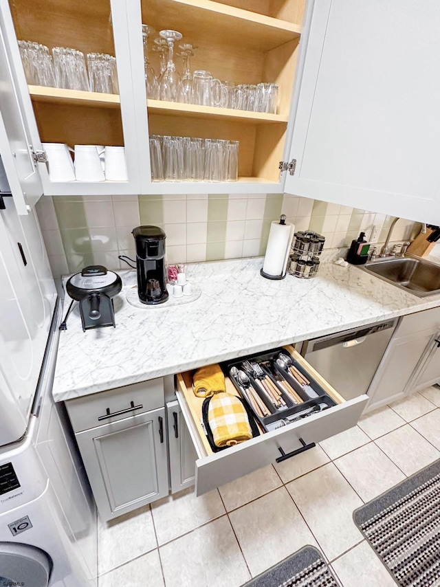 kitchen with light tile patterned floors, open shelves, decorative backsplash, a sink, and dishwasher