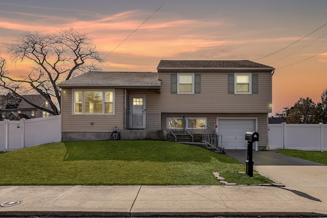 split level home featuring a garage, a shingled roof, fence, a yard, and concrete driveway