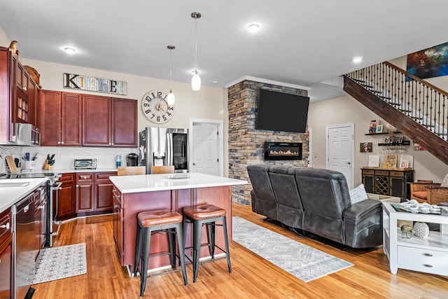 kitchen with reddish brown cabinets, open floor plan, stainless steel appliances, light countertops, and a kitchen bar