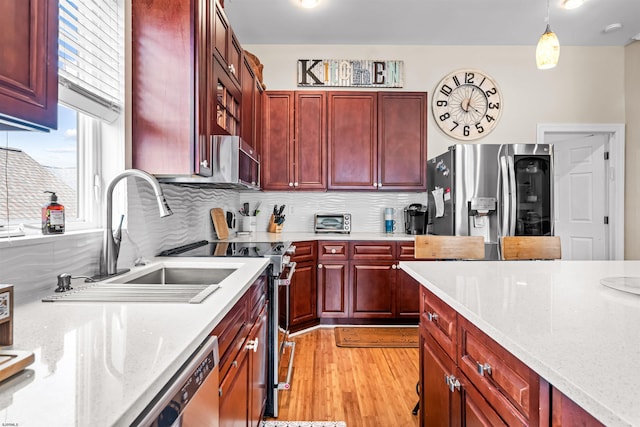 kitchen featuring stainless steel appliances, a sink, reddish brown cabinets, light wood finished floors, and pendant lighting