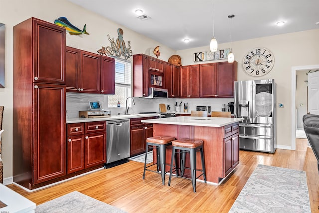 kitchen with stainless steel appliances, dark brown cabinets, light countertops, light wood-type flooring, and a kitchen bar