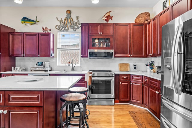 kitchen featuring light wood finished floors, backsplash, appliances with stainless steel finishes, a sink, and dark brown cabinets