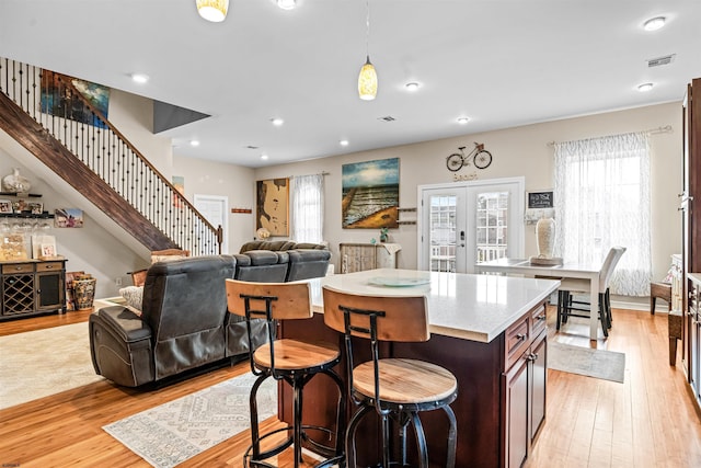 kitchen with a kitchen breakfast bar, light countertops, french doors, light wood finished floors, and decorative light fixtures