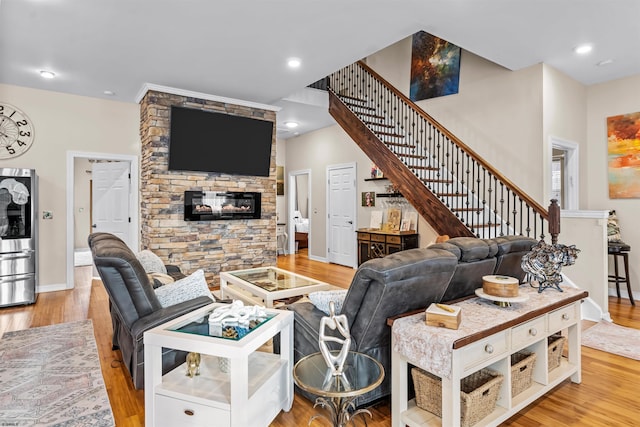 living room featuring stairs, a stone fireplace, baseboards, and wood finished floors