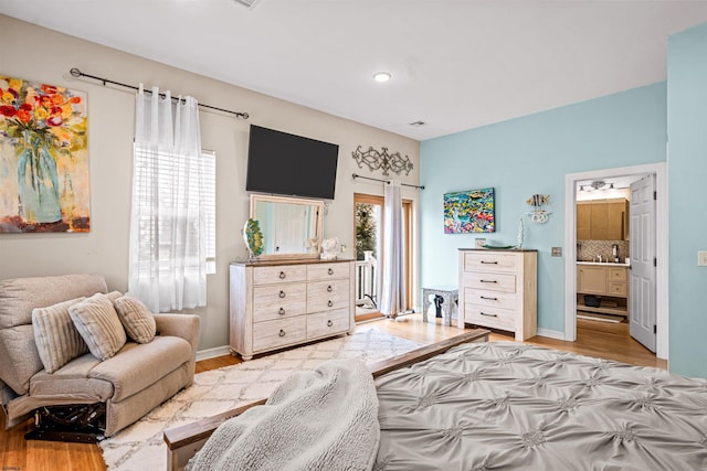 bedroom with baseboards, ensuite bath, light wood-style flooring, and access to exterior