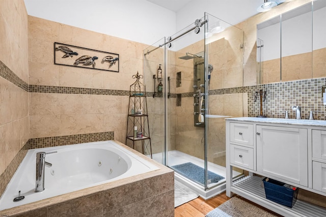 bathroom with a stall shower, tile walls, a jetted tub, and vanity