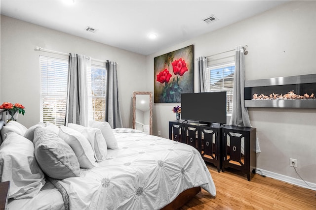 bedroom with multiple windows, wood finished floors, visible vents, and baseboards