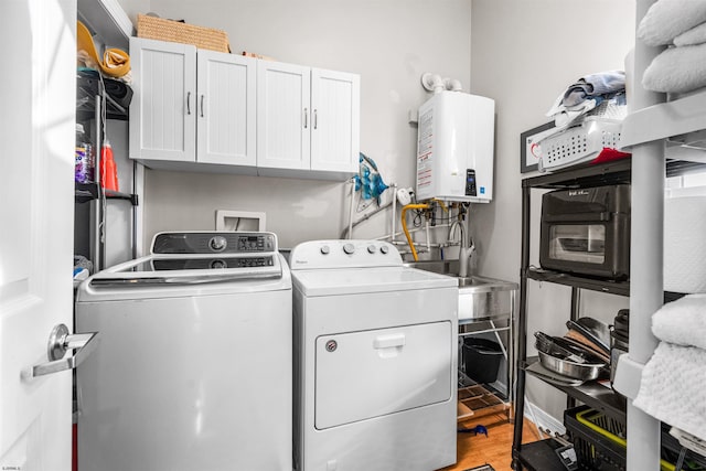 clothes washing area with water heater, light wood finished floors, washing machine and clothes dryer, and cabinet space