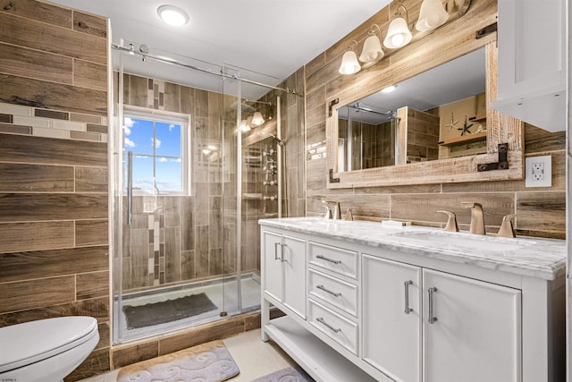 full bath with double vanity, a stall shower, toilet, a sink, and tile walls